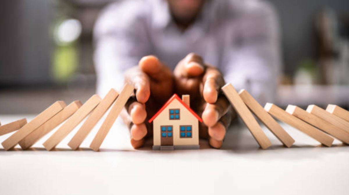 Person using their hands to shield a model house, symbolizing the protection and careful handling required during a home insurance claim process.