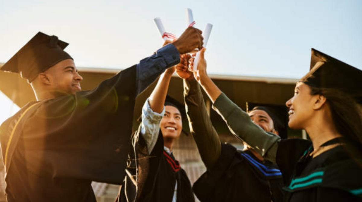 Group of graduate students celebrating their achievement, wearing caps and gowns, and joyfully holding their diplomas.